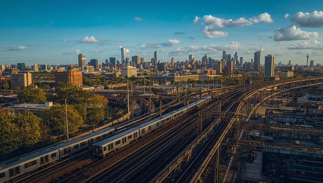 Gliding commuter train on elevated rail yard with New York City skyline at golden hour