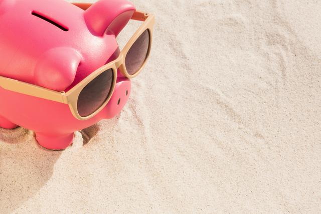 Close-up of piggy bank with sunglasses kept on sand at beach