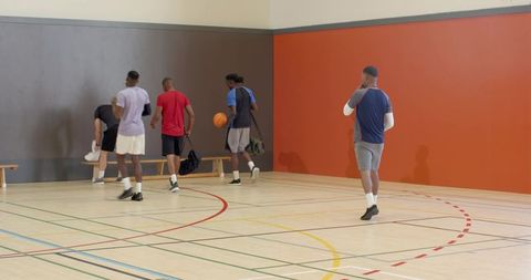 Five basketball players walking with duffel bags on indoor court before practice session
