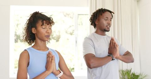 African american couple meditating at home wearing fitness watches and athletic gear