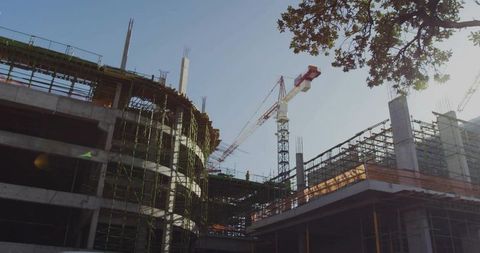 Constructing curved concrete building with scaffolding and tower cranes in urban daylight