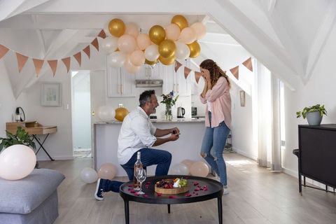 Romantic surprise proposal at home with balloons, wine, rose petals and bunting in loft
