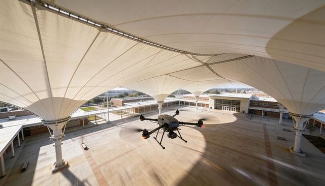 Hexacopter hovering under tensile canopy over campus courtyard during aerial survey