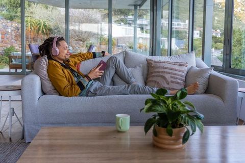 Relaxing african american man listening to music on couch in modern glass-wall living room