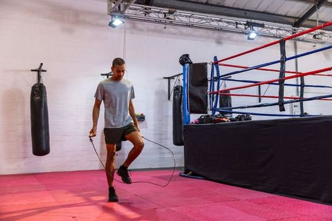 Young man skipping rope by boxing ring training cardio agility wearing grey t-shirt and shorts