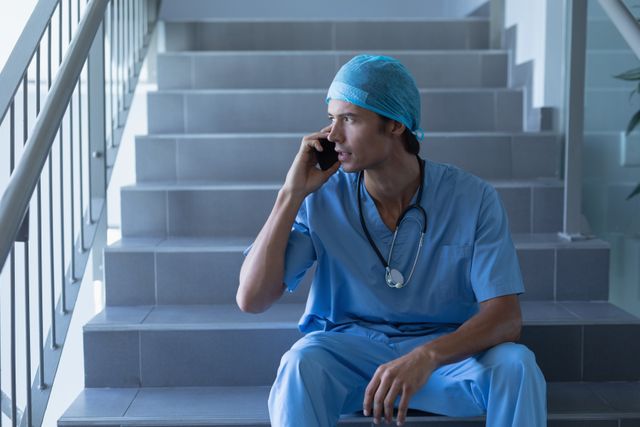 Male Surgeon Talking on Mobile Phone While Sitting on Hospital Stairs - Download Free Stock Photos Pikwizard.com