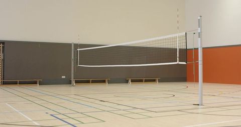 Indoor volleyball court featuring net on white posts, hardwood multipurpose floor and markings