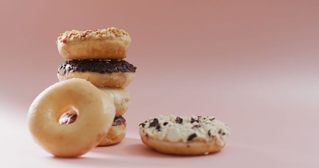 This image showcases a variety of mouth-watering donuts, neatly stacked and displayed on a soft pink background. Ideal for use in bakery promotions, dessert blog posts, food advertisements, and social media posts targeting food enthusiasts. The bright and appealing colors make it perfect for attracting attention from sweet-tooth customers.