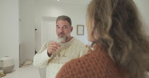 Senior Man Enjoying Wine Conversation with Middle-Aged Woman at Kitchen Counter