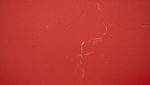 Crimson plaster wall showing hairline crack revealing lighter undercoat texture