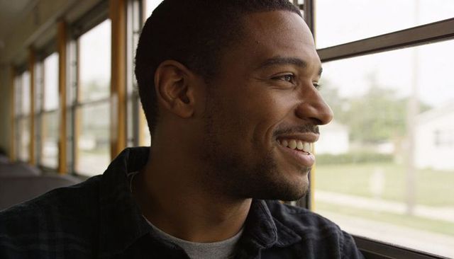 Young man smiling and gazing out bus window during sunny suburban commute