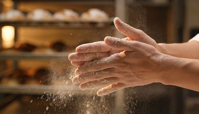Baker clapping flour-covered hands creating dramatic flour cloud over baking racks