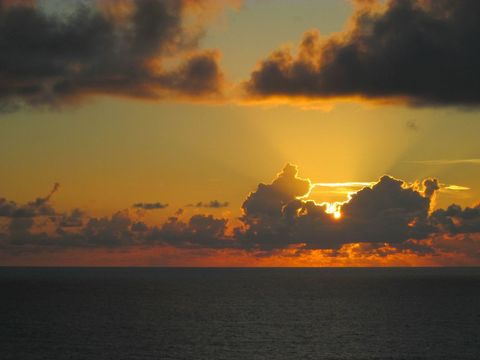 Golden sunrise breaking through dark clouds over calm ocean horizon
