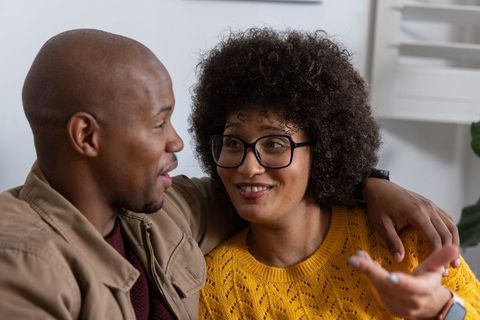 Couple sharing warm conversation on couch, woman wearing glasses, man with arm around