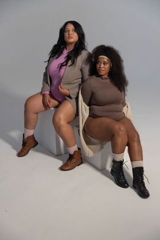 Diverse plus-size models posing in bodysuits with blazers and boots on white studio cubes