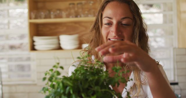 Smiling caucasian woman touching plant in cottage kitchen. healthy living, close to nature in off grid rural home.