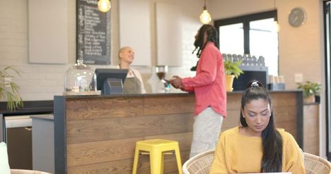 Urban cafe coworking scene with barista serving customer and woman working on laptop