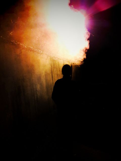 Silhouette of a person standing in a tunnel with dramatic backlighting. Intense light source behind the individual creates a mysterious and atmospheric effect, with the appearance of smoke or mist enhancing the mood. Ideal for themes related to mystery, suspense, solitude, urban exploration, or atmospheric lighting techniques.