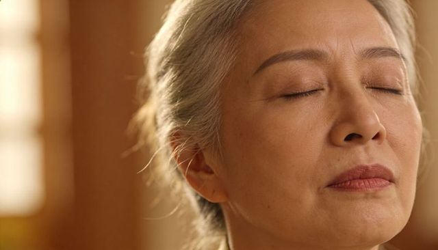 Senior asian woman resting with closed eyes soaking warm window light for meditation