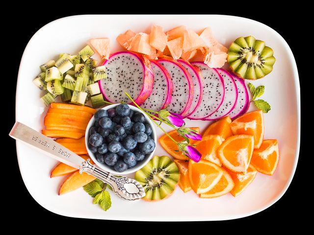 Vibrant fresh tropical fruits arranged artistically on a white plate. Slices of dragon fruit, kiwi, orange, papaya and a bowl of blueberries are neatly placed, making it visually appealing. Ideal for use in contexts related to healthy eating, nutrition, gourmet dishes, food styling, and culinary arts. Perfect for blog posts, menu design, social media content, or health-related promotions.