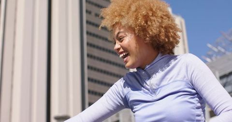 Joyful woman laughing and leaning in sunny urban plaza wearing purple workout top downtown