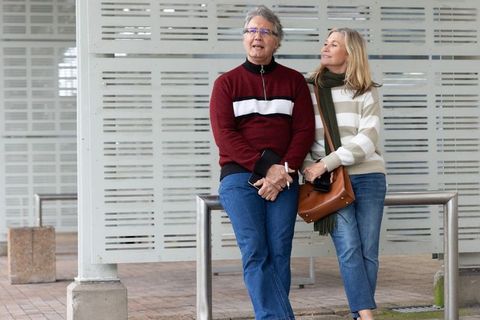 Mature couple leaning on railing enjoying relaxed urban plaza stroll wearing sweaters