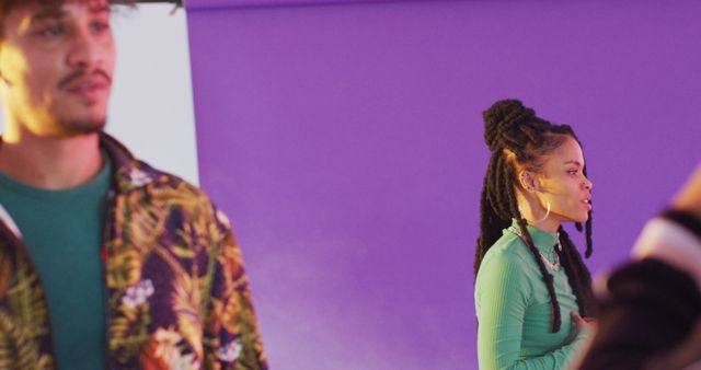 Two people expressing themselves against a vibrant purple backdrop. Ideal for use in contexts related to individuality, modern fashion, cultural expressions, and creativity. The purple background adds an artistic touch, making it suitable for advertisements, social media posts, and artistic projects highlighting urban culture and trends.