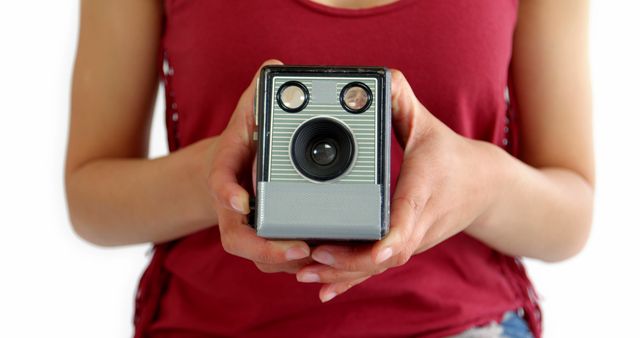 This image shows a woman wearing a burgundy tank top, holding a vintage camera tightly with both hands against a white background. Ideal for use in articles or blogs about retro photography, hobbies, or the resurgence of analog film. It can also be useful for marketing or promotional materials involving nostalgic themes or vintage camera collections.