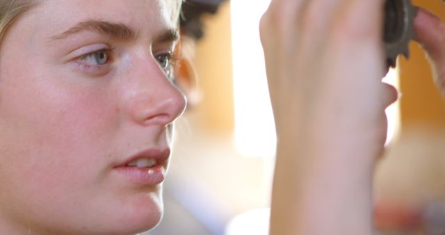 Young woman examines mechanical gear with intense focus. Ideal for content on Technological innovation, female engineers, STEM education, mechanical engineering, and precision tasks.