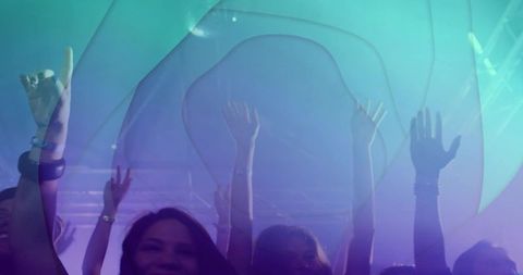Nightclub crowd raising hands and cheering under teal purple lighting with stage projections