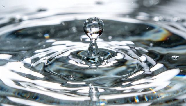 Crystal water droplet rising on column with concentric ripples and iridescent highlights