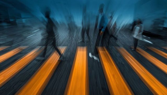 Motion-blurred commuters walking across orange crosswalk at night in urban cityscape
