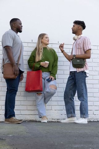 Friends chatting on city sidewalk with coffee and red shopping bag, casual urban conversation