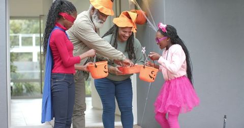 Black family celebrating halloween on porch sharing pumpkin buckets and treats