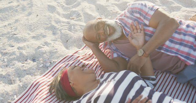 Senior couple lying on a striped beach blanket, smiling and enjoying each other's company. Ideal for themes surrounding love, relationships, retirement, and outdoor lifestyles. Can be used for promotional materials, health and wellness topics for seniors, or travel and leisure content.