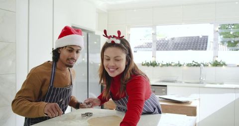 Couple baking christmas cookies together in bright modern kitchen wearing santa hats and aprons