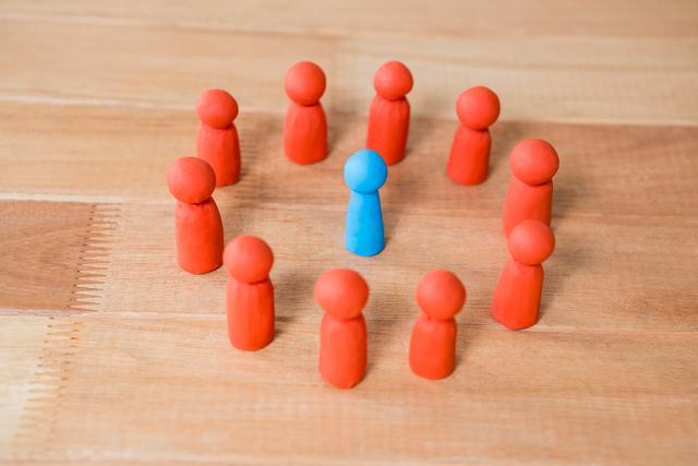Conceptual image showing a blue figurine standing out among a group of red figurines on a wooden surface. This image can be used to represent themes of individuality, uniqueness, leadership, and standing out in a crowd. It is suitable for articles, presentations, and marketing materials focusing on diversity, inclusion, and group dynamics.