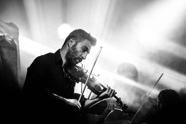 Passionate violinist engrossed in performance on stage, illuminated by spotlight in black and white setting. Image ideal for use in articles or promotions related to live music events, concerts, classical music, musicians, music performances, or artistic dedication.
