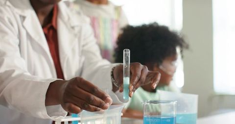 African american science teacher pouring test tube into beaker teaching teen students
