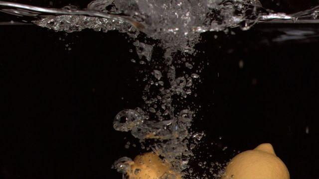 Captivating shot of two lemons creating an explosion of bubbles as they drop into water against a black background. Perfect for use in food and beverage commercials, health and lifestyle blogs, or as visual content emphasizing freshness and purity.