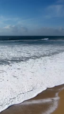 Approaching swell exploding into foamy surf on sandy shoreline vertical ocean video