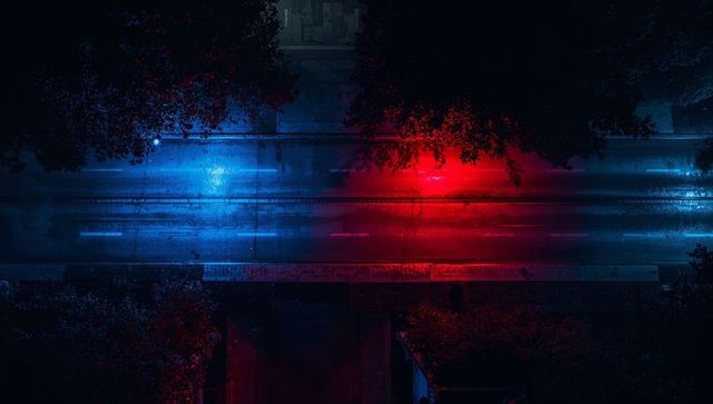 Neon night road glowing with red and blue light pools over wet reflective asphalt, aerial