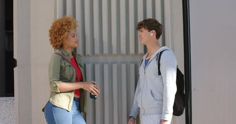 Urban college friends chatting on sidewalk with backpack, hoodie, jacket and takeaway cup