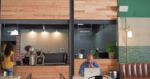 Man working on laptop in industrial wood cafe with espresso counter and greenery