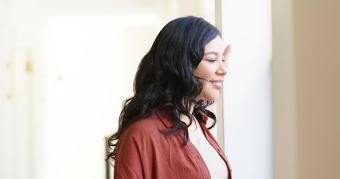 Woman gazing out window in sunlit minimalist interior, serene casual portrait