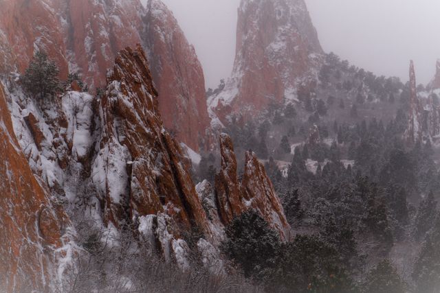 Beautiful winter scene featuring tall, rugged rocks covered in snow amidst foggy atmosphere. Ideal for nature documentaries, winter travel promotions, outdoor adventure blogs, and serene landscape art prints showcasing the beauty of natural formations in a winter setting.