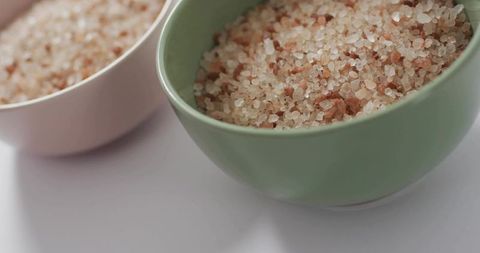 Holding green ceramic bowl filled with himalayan pink salt crystals on white countertop