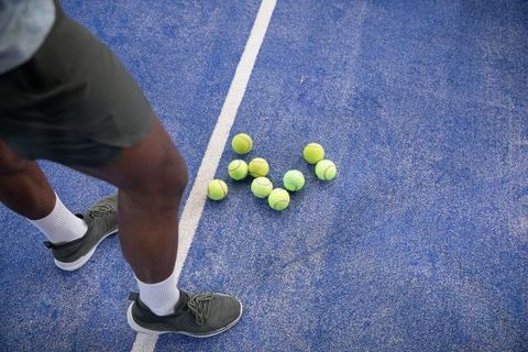 African american player standing beside cluster of tennis balls on blue court surface