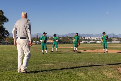 Mature Coach Coaching Baseball Team on Sunny Field During Infield Practice Session