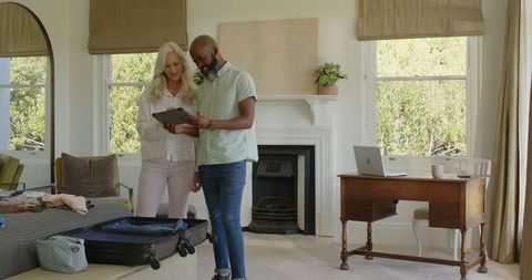 Couple packing suitcase discussing travel plans with tablet at home